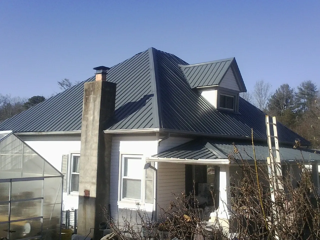 Dark blue standing seam metal roof on a white farmhouse with dormer — Slate & Tile Roof Repair by Roofing Brothers in Adelanto