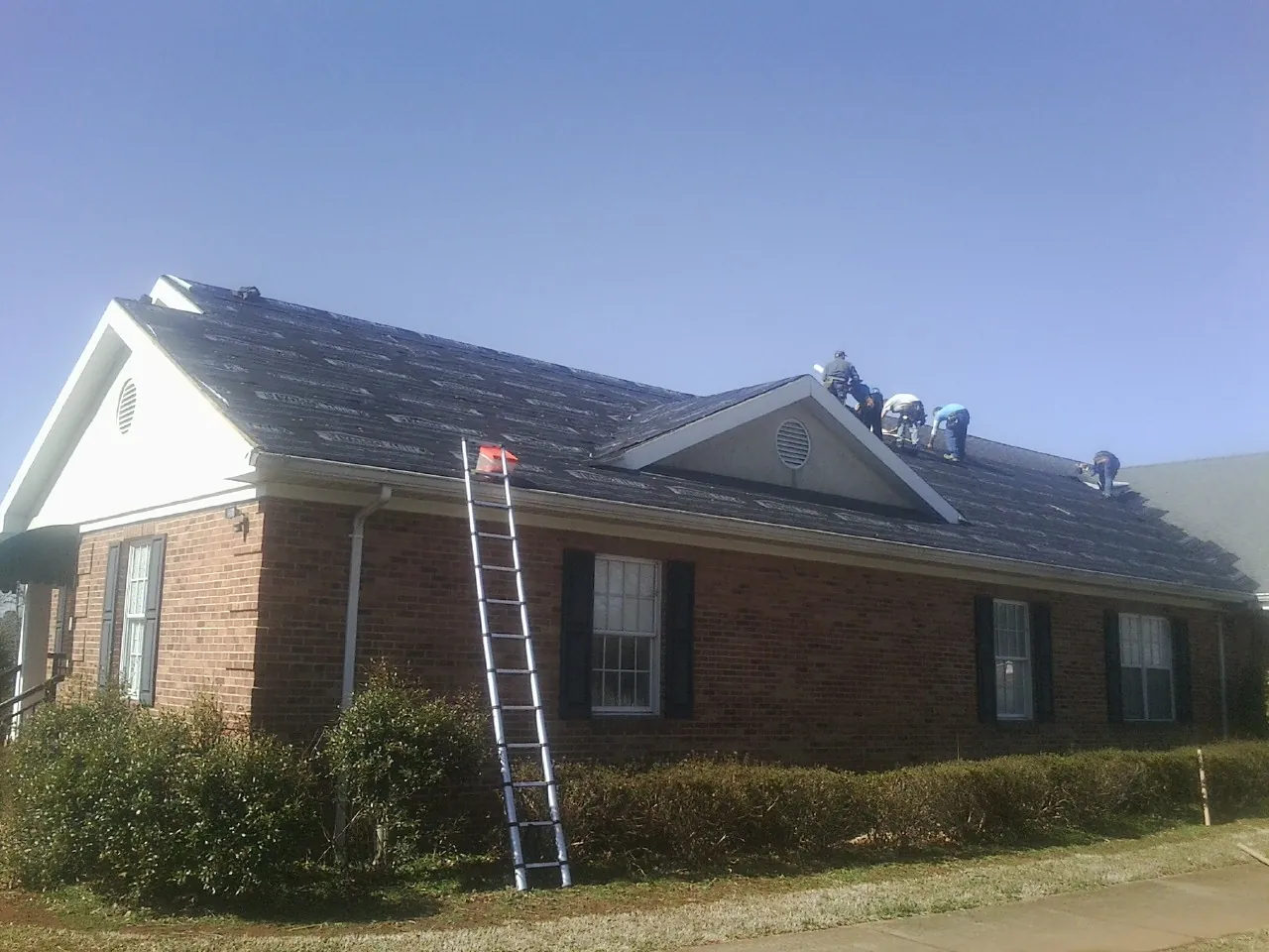 Crew tearing shingles off a brick ranch roof with a ladder set — Emergency Roof Repair work by our crew in Adelanto