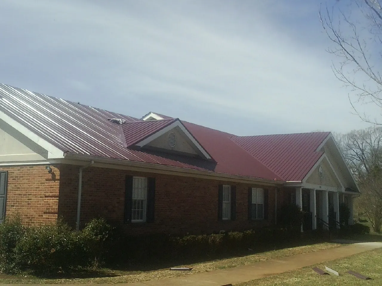 Red metal roof with gabled entries on a long brick building, from a Hail Damage Roof Repair job in Adelanto