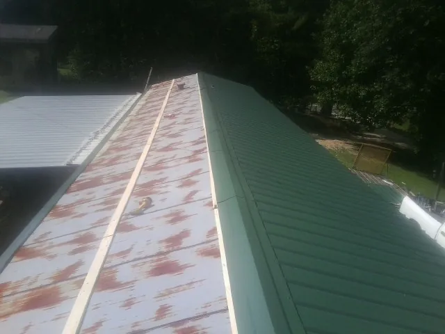 Old rusted panels beside newly installed green metal roofing — Wind Damage Roof Repair by Roofing Brothers in Adelanto
