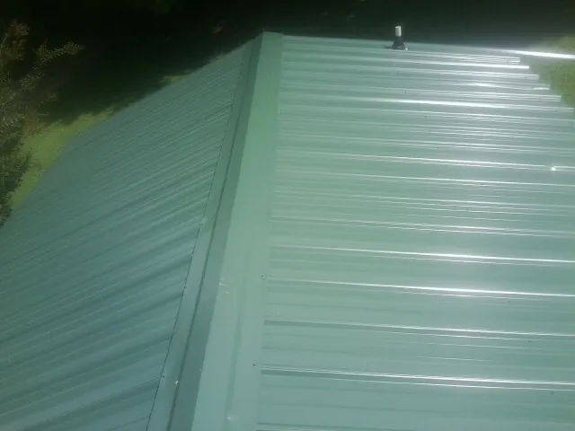 New green metal panels meeting at the ridge of a roof — Flat Roof Repair work by our crew in Adelanto