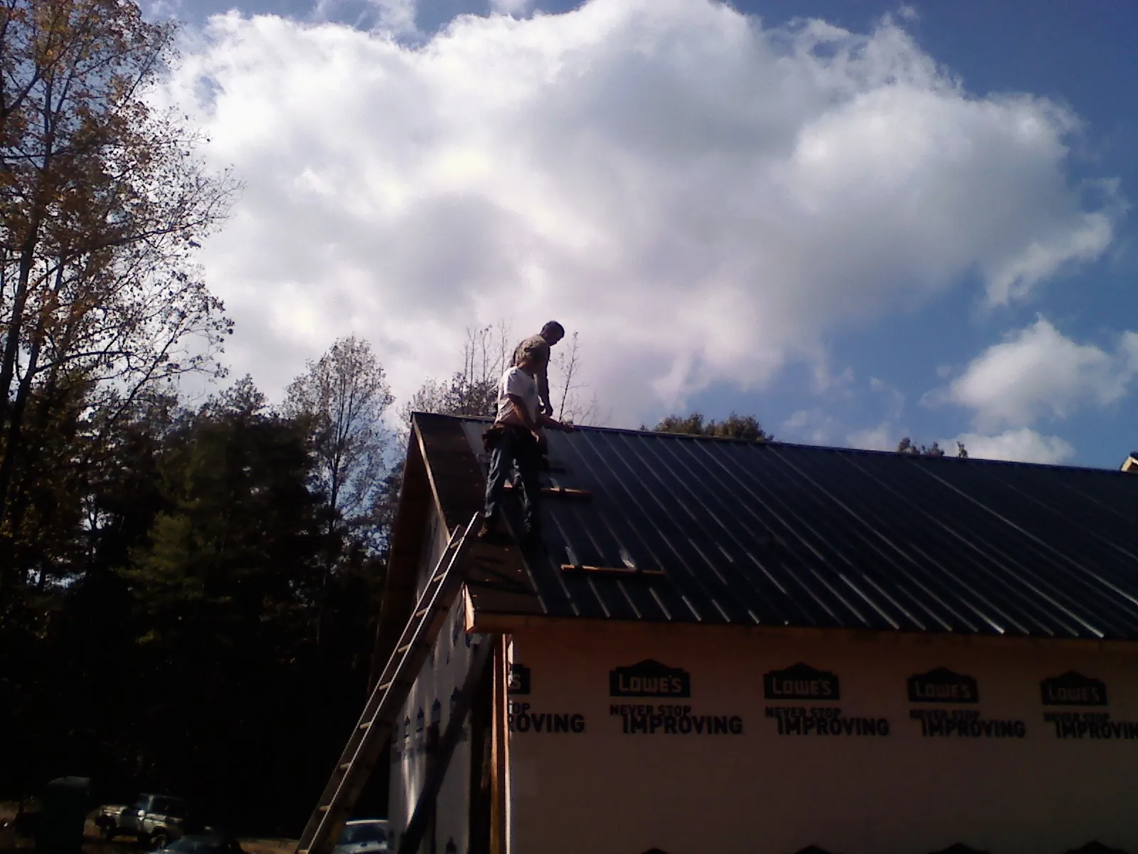 Roofer fastening dark metal panels high against a cloudy sky, from a Roof Inspection job in Adelanto